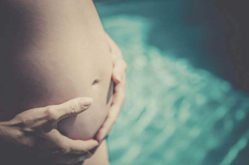 A pregnant woman holding her bare belly.