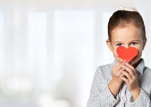 A young girl holding a paper heart over her face and smiling.