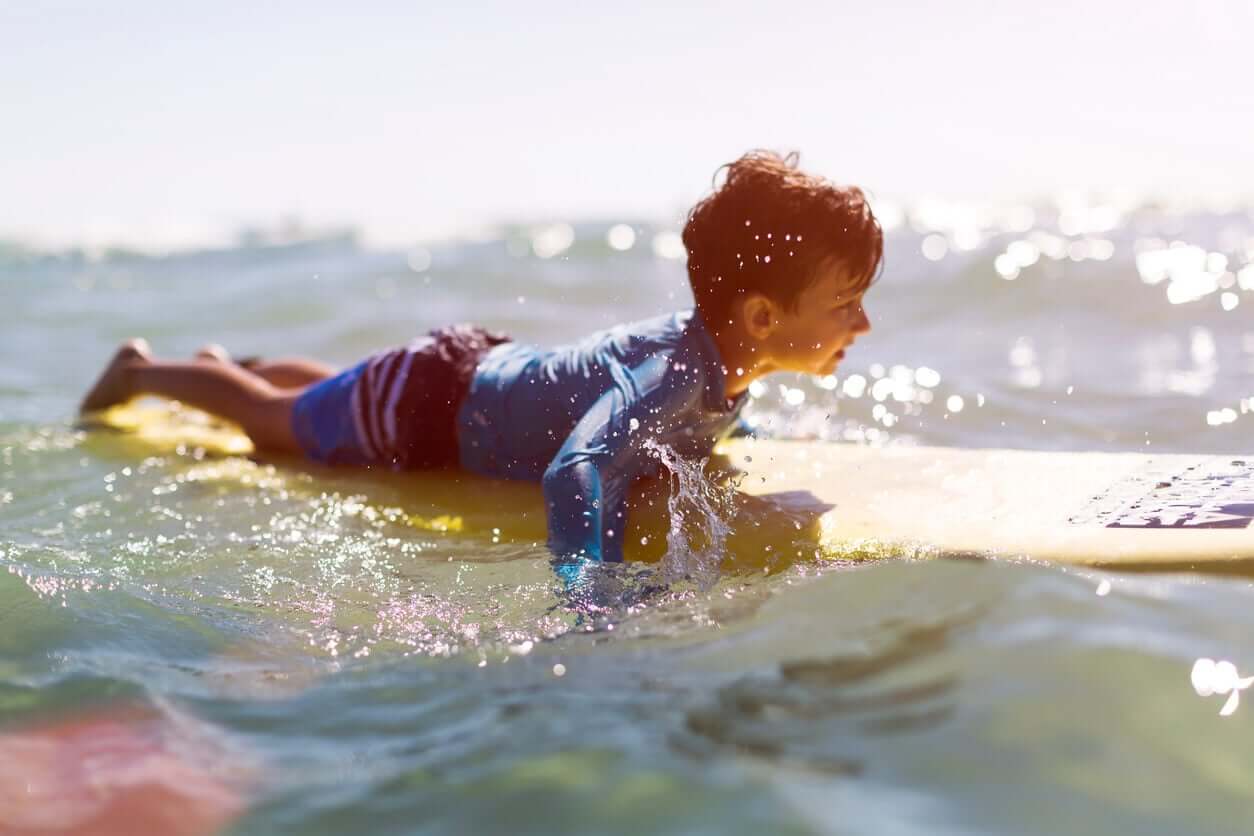 A little boy lying on a surf board in the water.