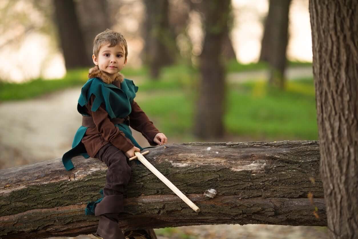 A little boy dressed as a medieval knight sitting on a log and holding a sword.