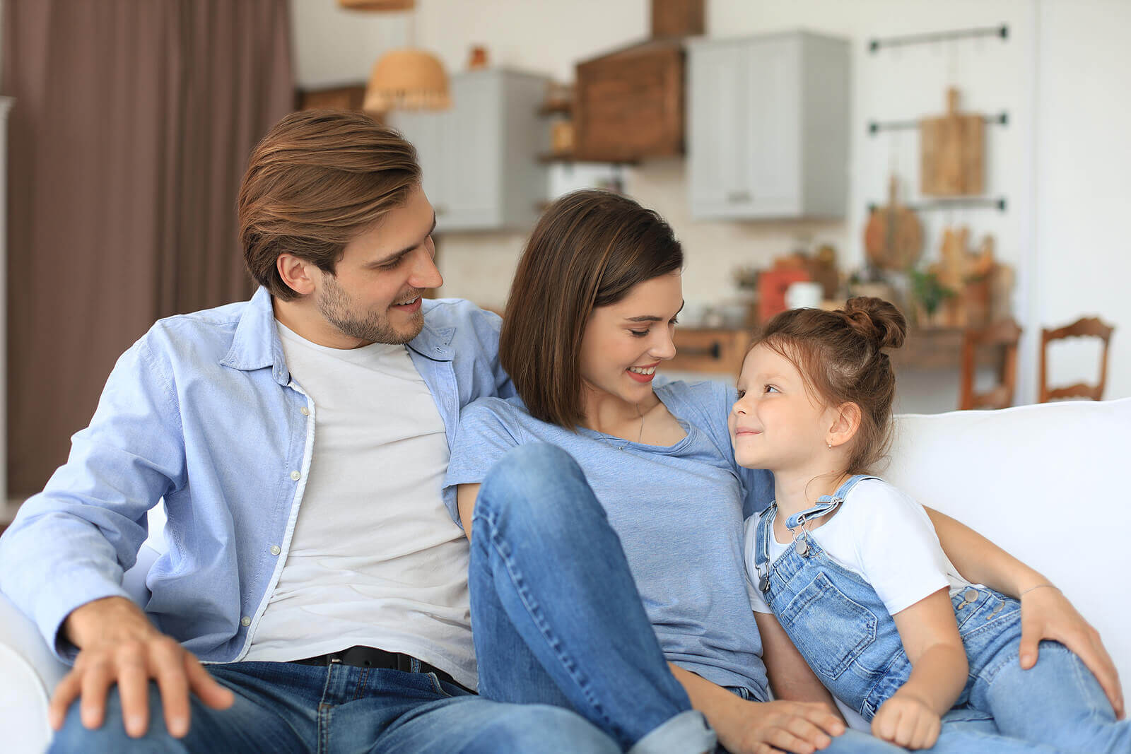 A mother and father sitting on the couch with their daughter.