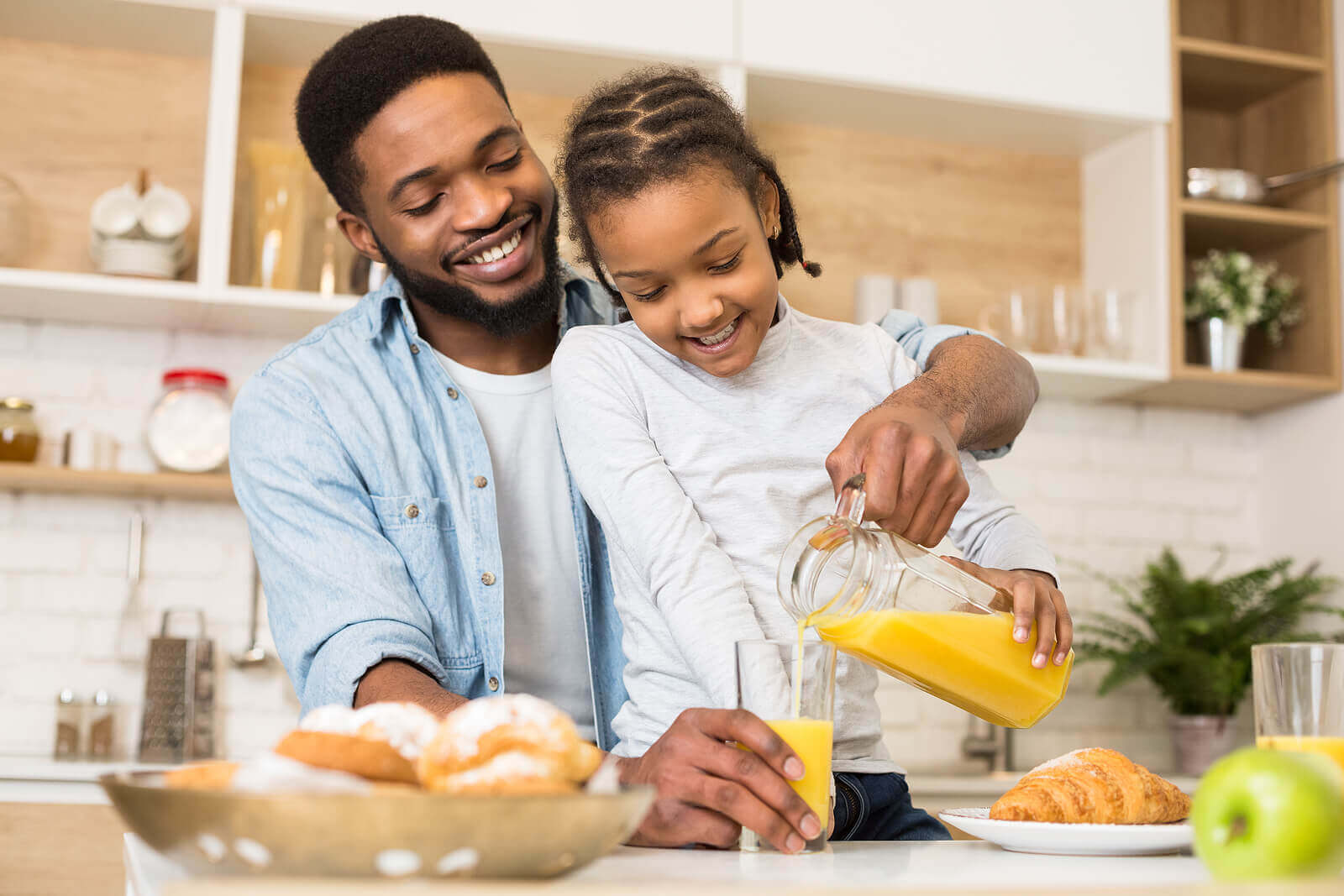 A father helping his daughter pour orange juice.