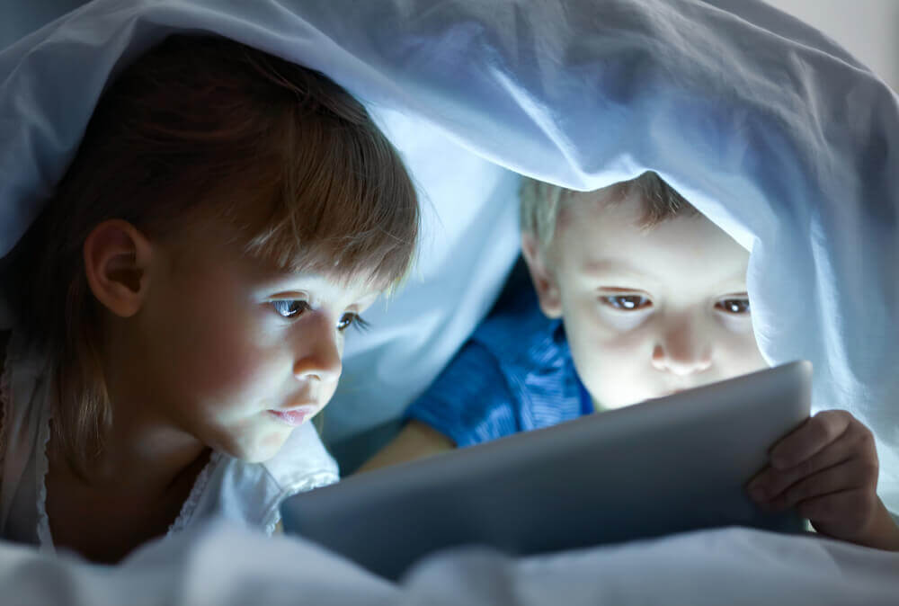 A little boy and girl looking at a tablet in bed.