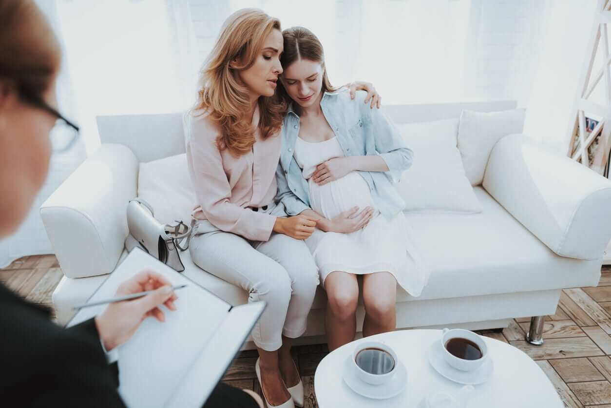 A woman with her arm around a pregnant woman's shoulder in a therapy session.