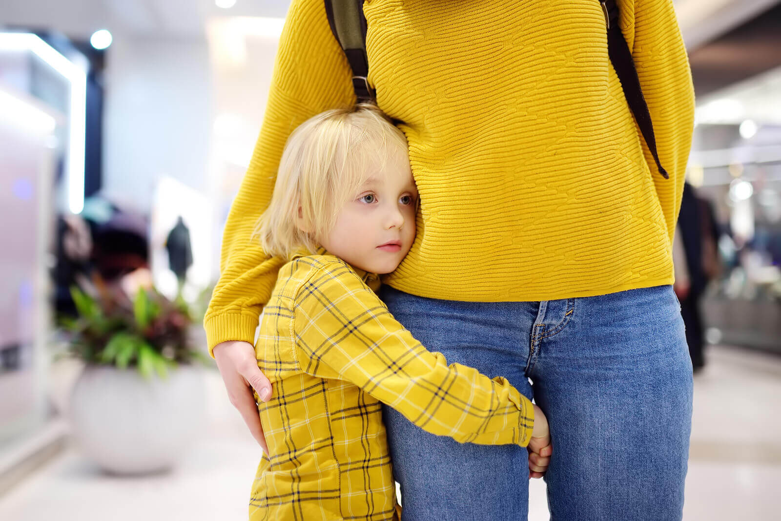 A young boy hugging his mom's leg.