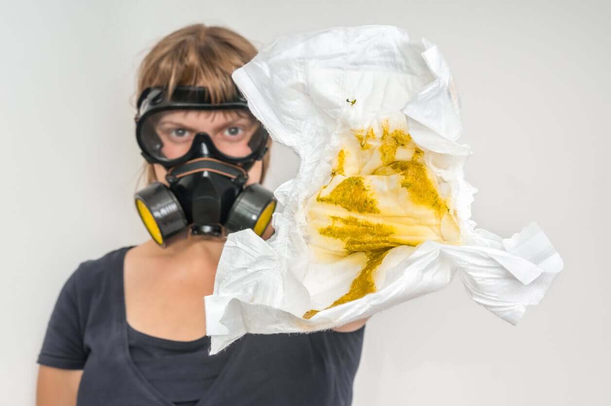 A woman wearing a gas mask holding a poopy diaper.