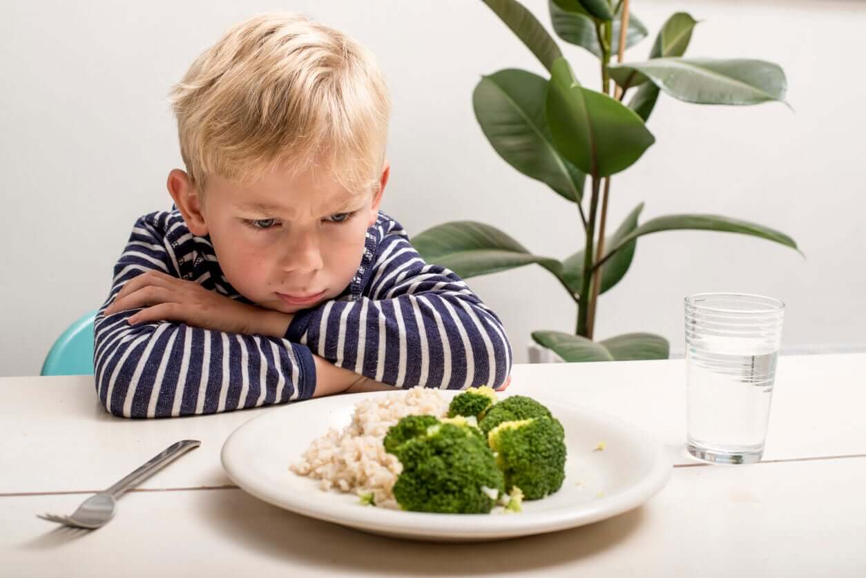 En ung pojke som stirrar argt på en tallrik med ris och grönsaker.
