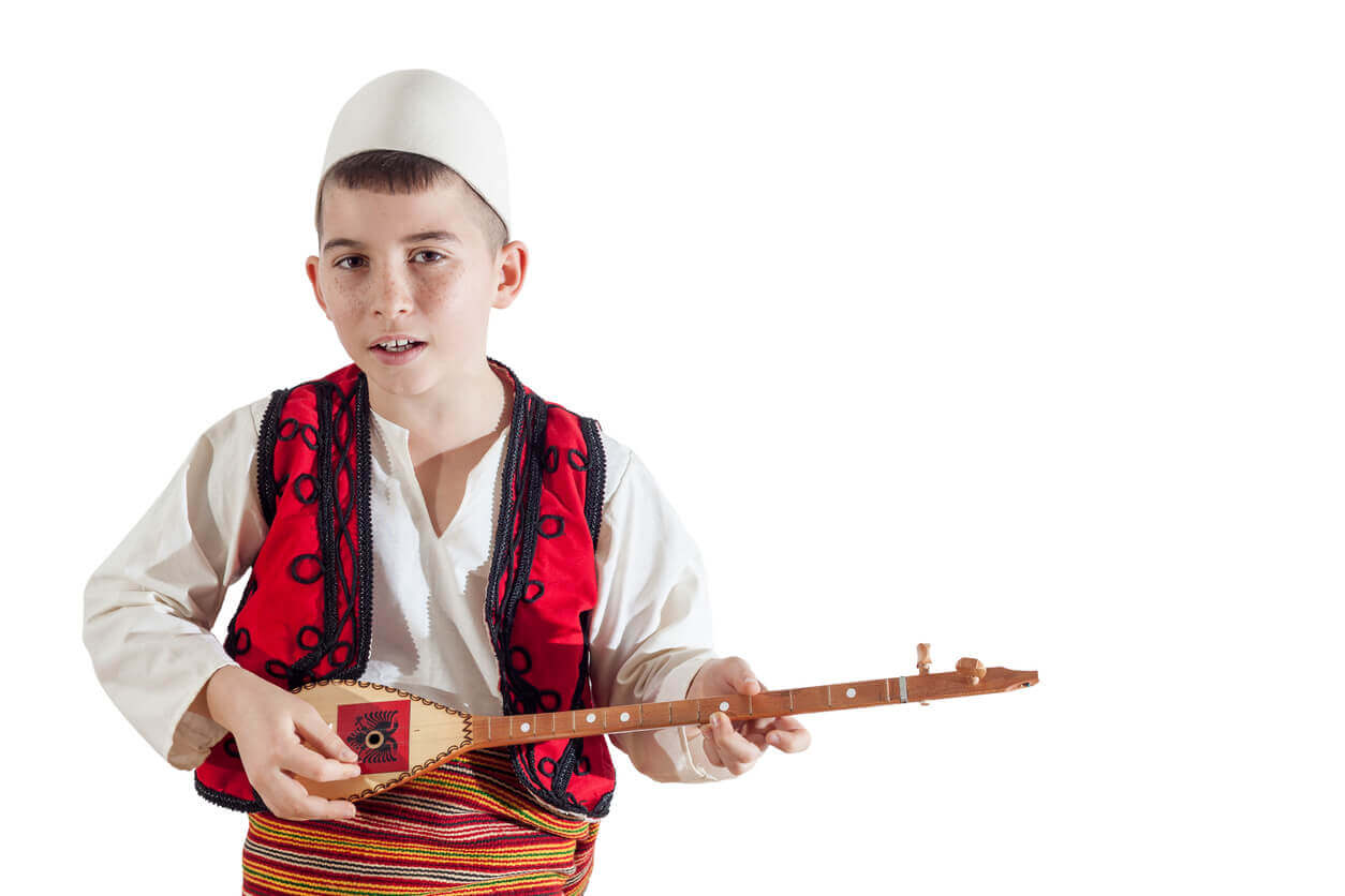 An Albanian boy in traditional dress playing a traditional instrument.