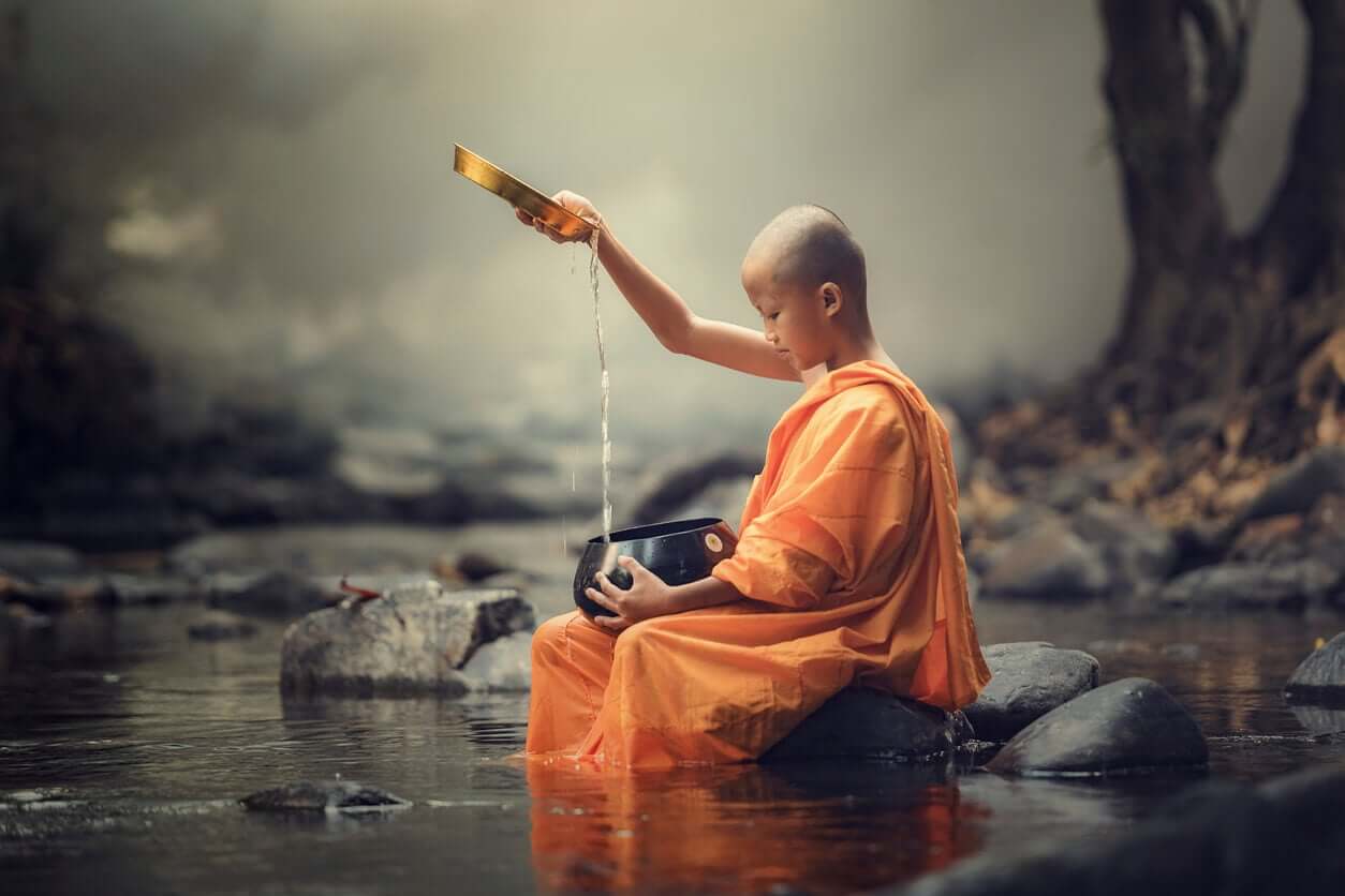 A young Buddhist monk pouring water from a stream into a pot.