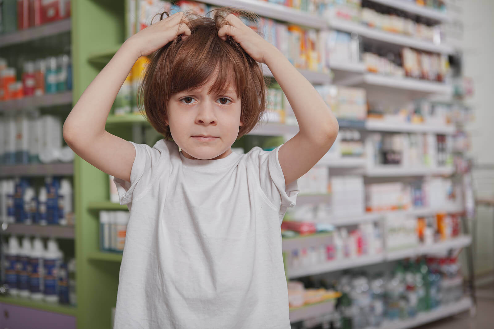 A little boy scrathing his head in a pharmacy.