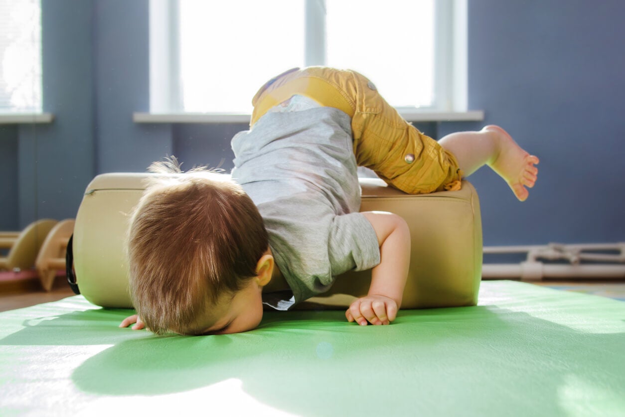 A toddler falling on his face while trying to crawl over a cushion.