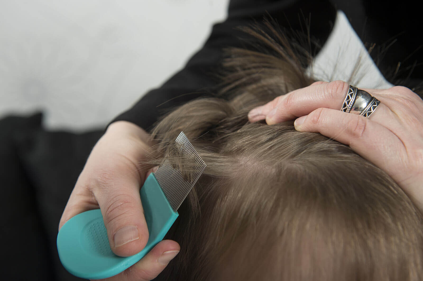 A woman removing lice from a child's hair with a fine comb.