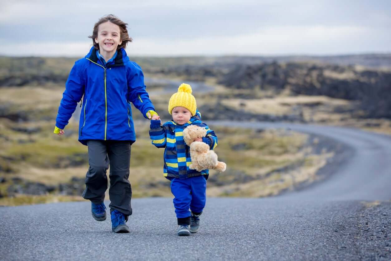 Two young boys wearing yellow and blue, running along a road in Iceland.