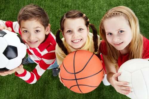 Three children holding a soccer ball, a basketball, and a volleyball.