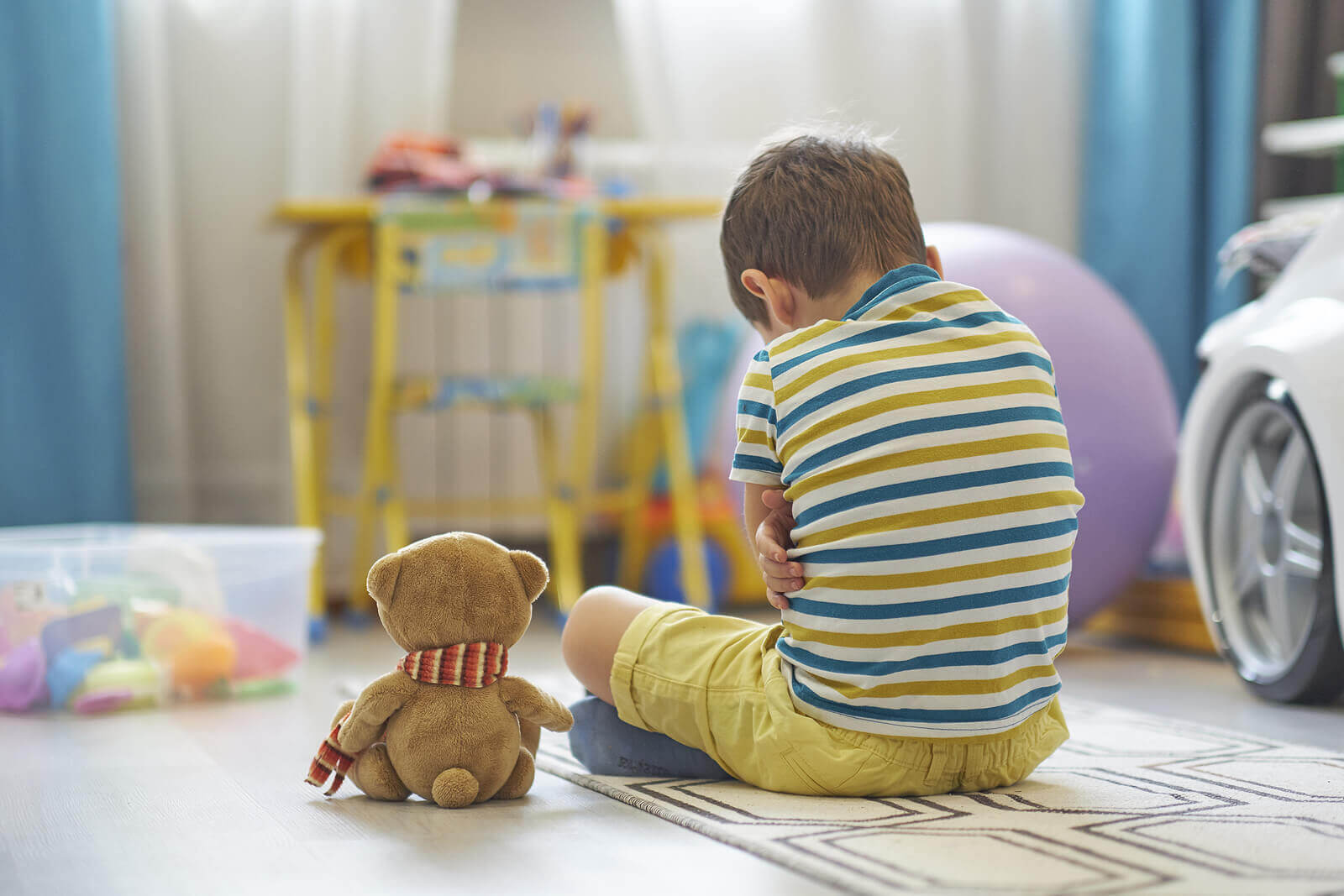 A child sitting on the floor with his arms crossed looking upset.