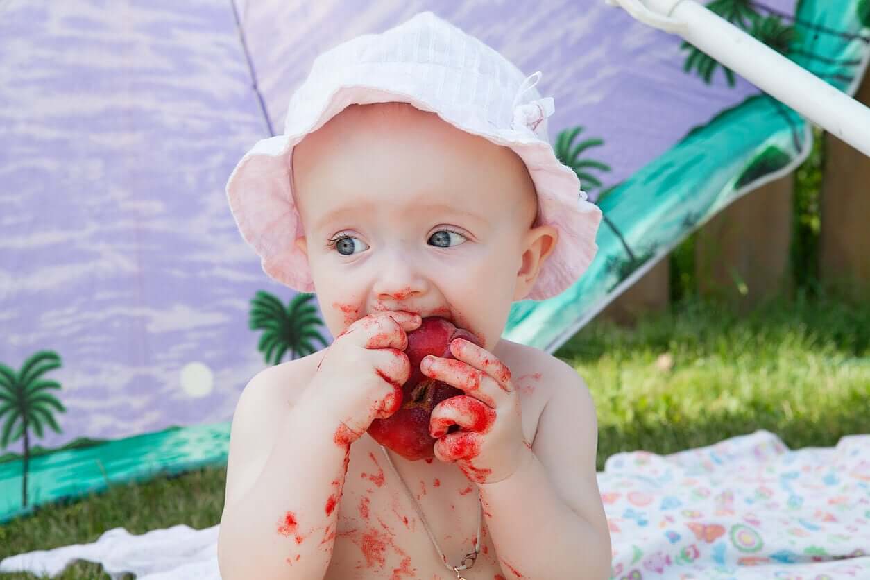 A baby eating fruit and getting it all over herself.