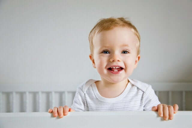A baby boy standing in his crib and smiling.