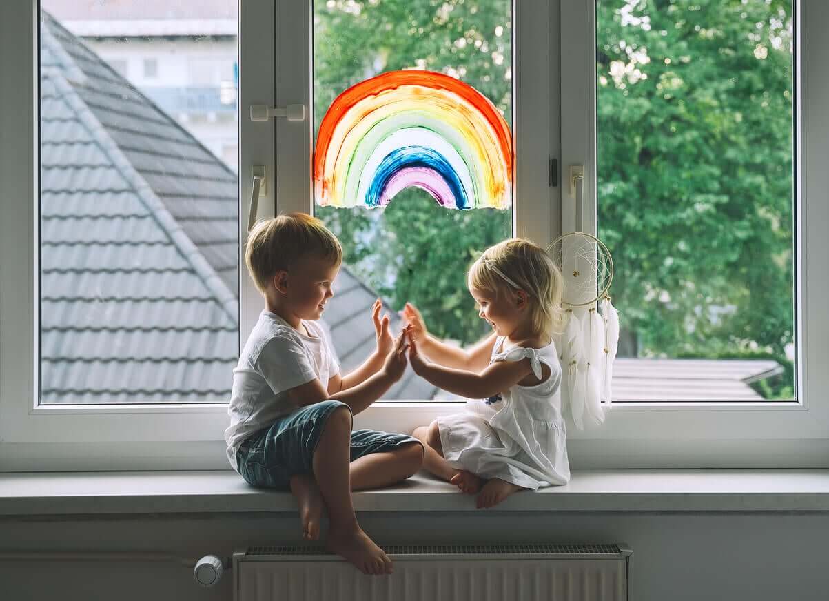 To børn leger foran vindue med regnbue på