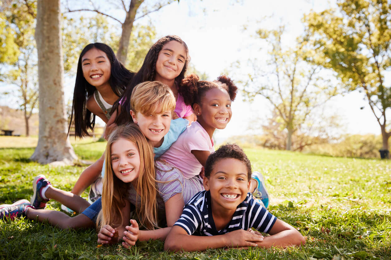 A multicultural group of children piled on top of one another in a park.
