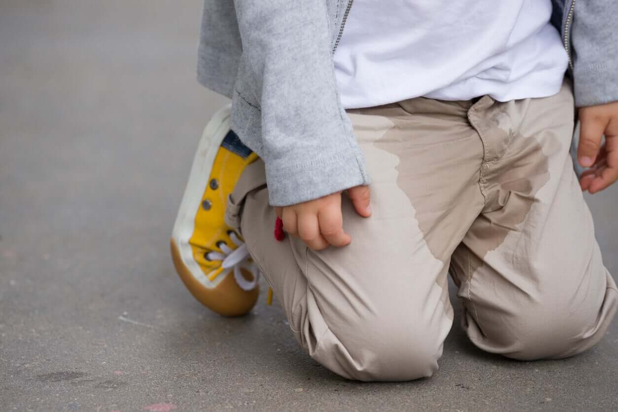 Ett litet barn på knä på golvet efter att ha kissat ner sina byxor.