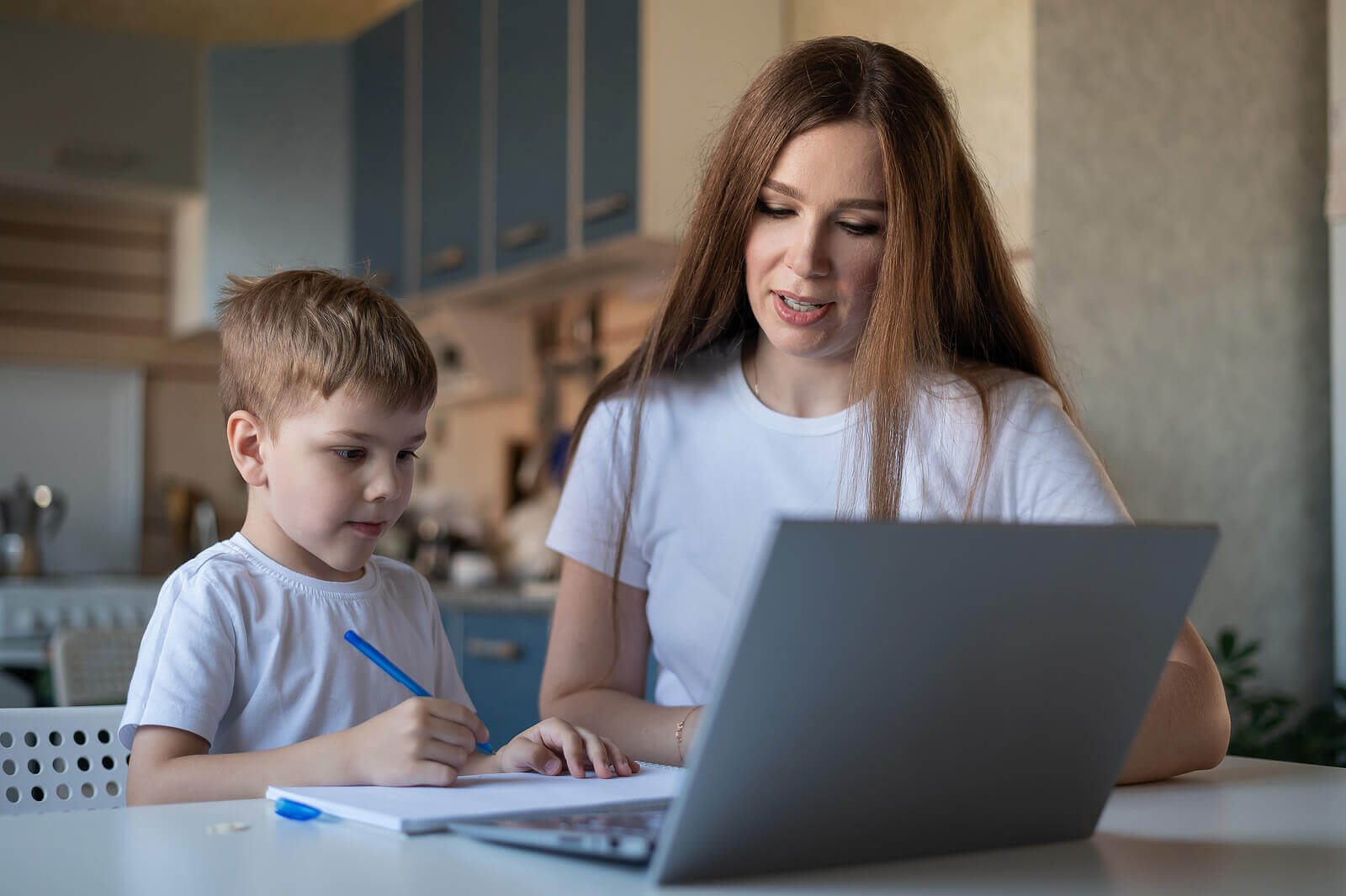 En mor og hennes sønn bruker en bærbar datamaskin mens han gjør lekser.