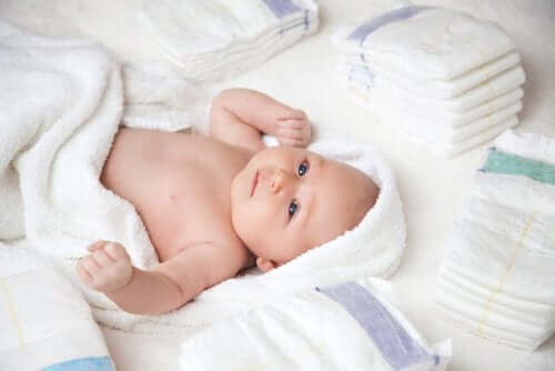 En baby insvept i en handduk omgiven av engångsblöjor.