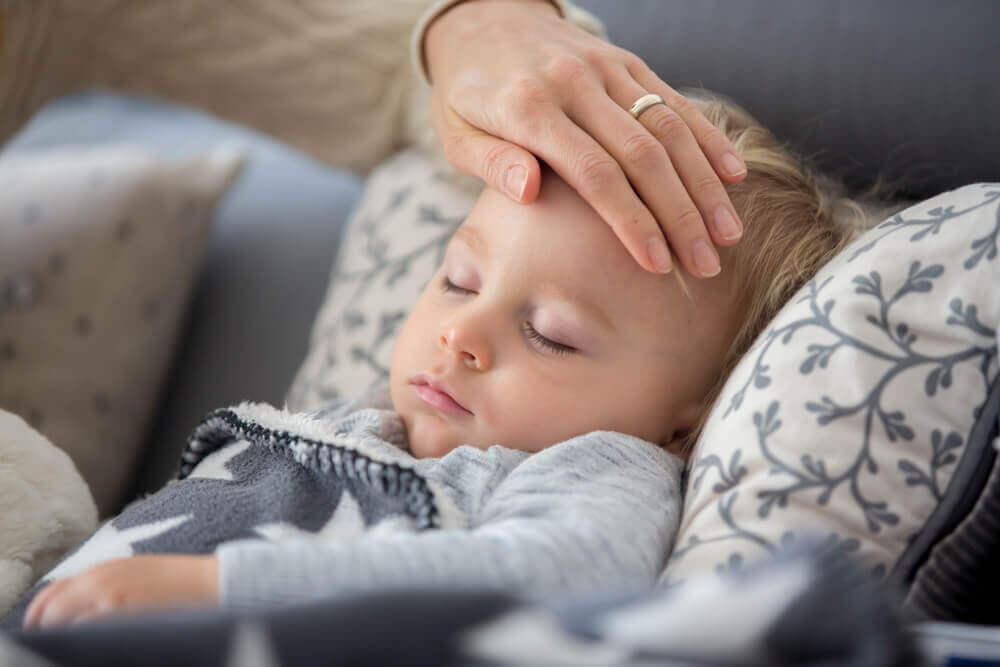 En mor kjenner på pannen til den sovende babyen med hånden.