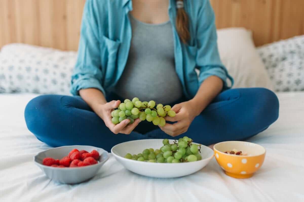 En gravid kvinna som äter vindruvor, bär och nötter.