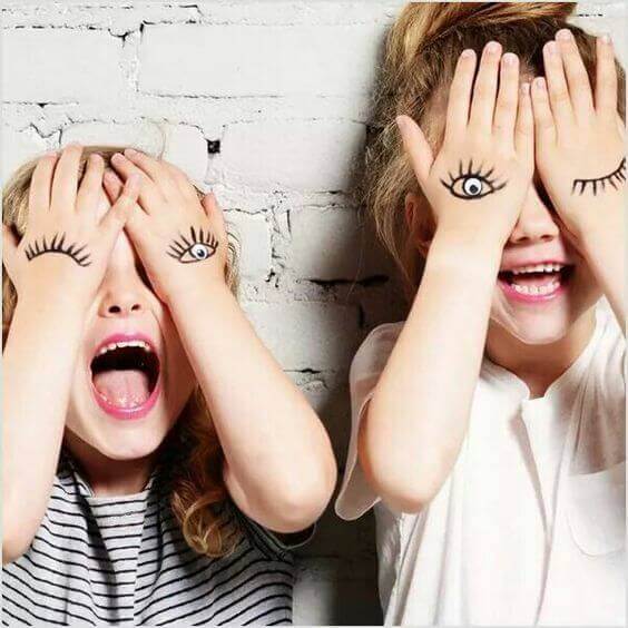 Children covering their eyes with their hands, which have eyes painted on them.