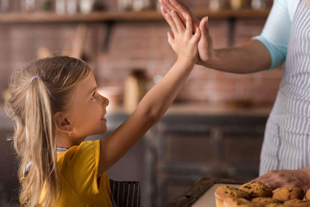 A little girl giving her mother a high five as they bake in the kitchen.