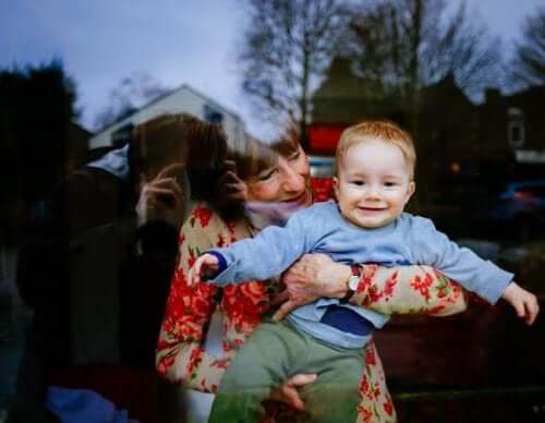 A mother holding her smiling grandson in front of a large window.