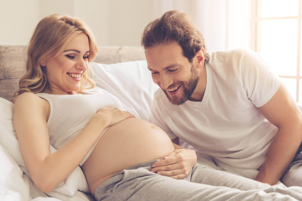 A man smiling while looking at his partner's pregnant belly.