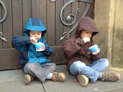 Two little boys sitting on the sidewalk eating ice cream.