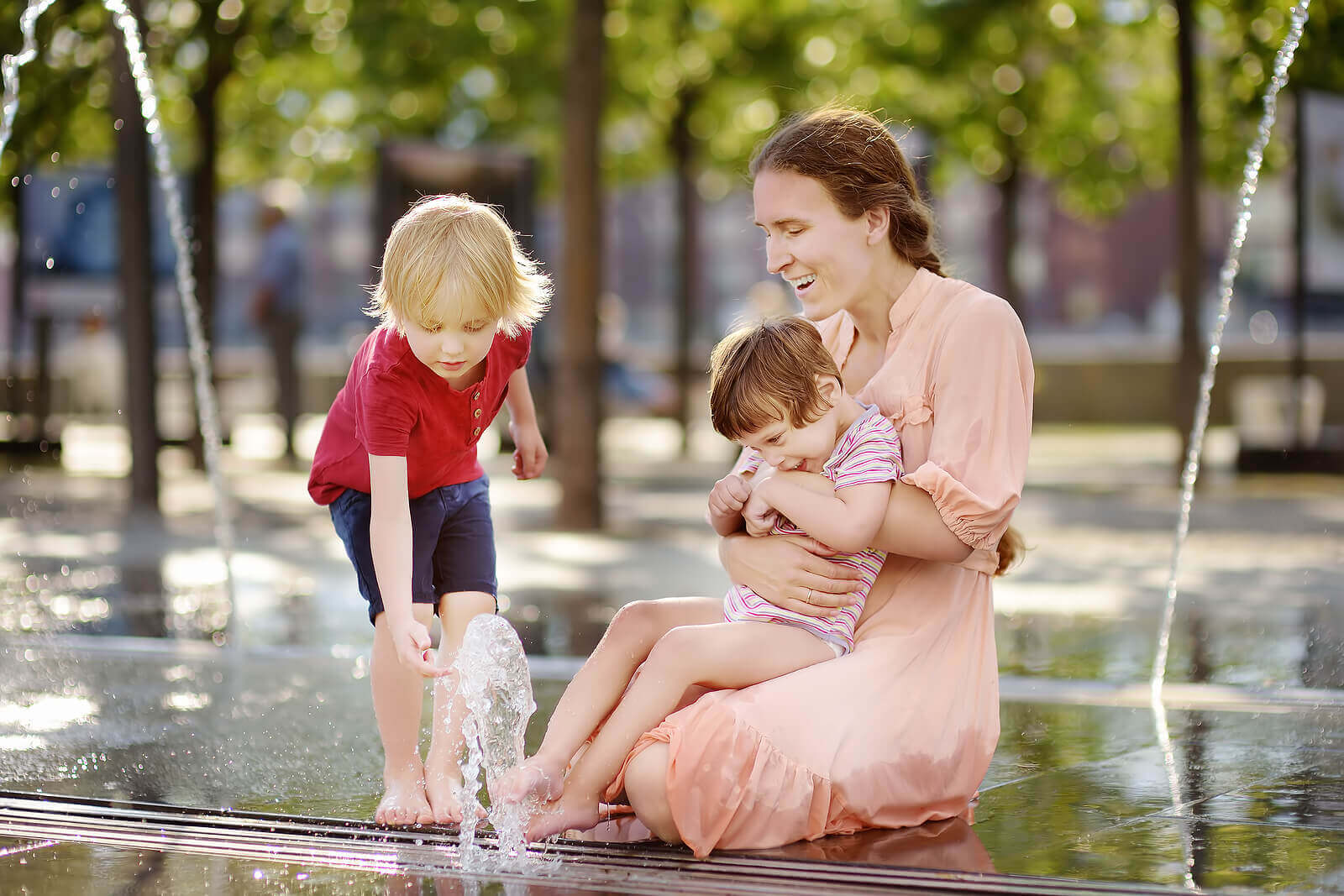 A mother playing in a fountain with her children.