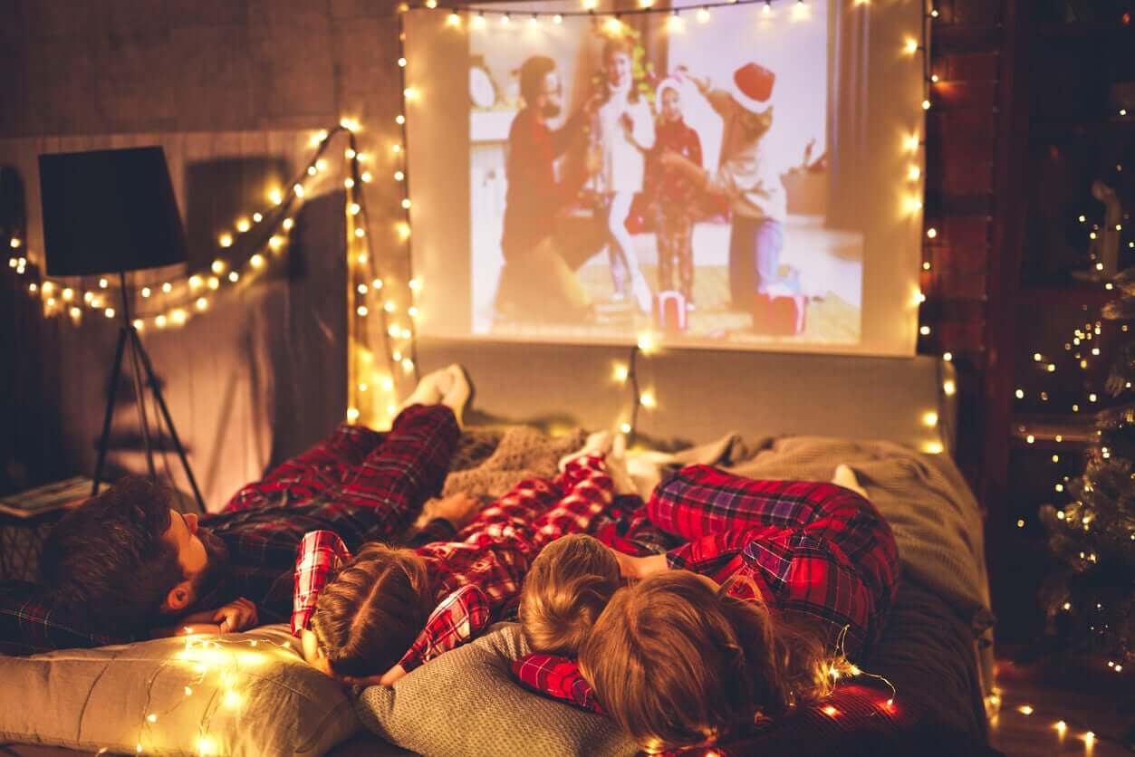 Barn som ligger på madrasser på gulvet og ser på en julefilm på en projeksjonsskjerm.