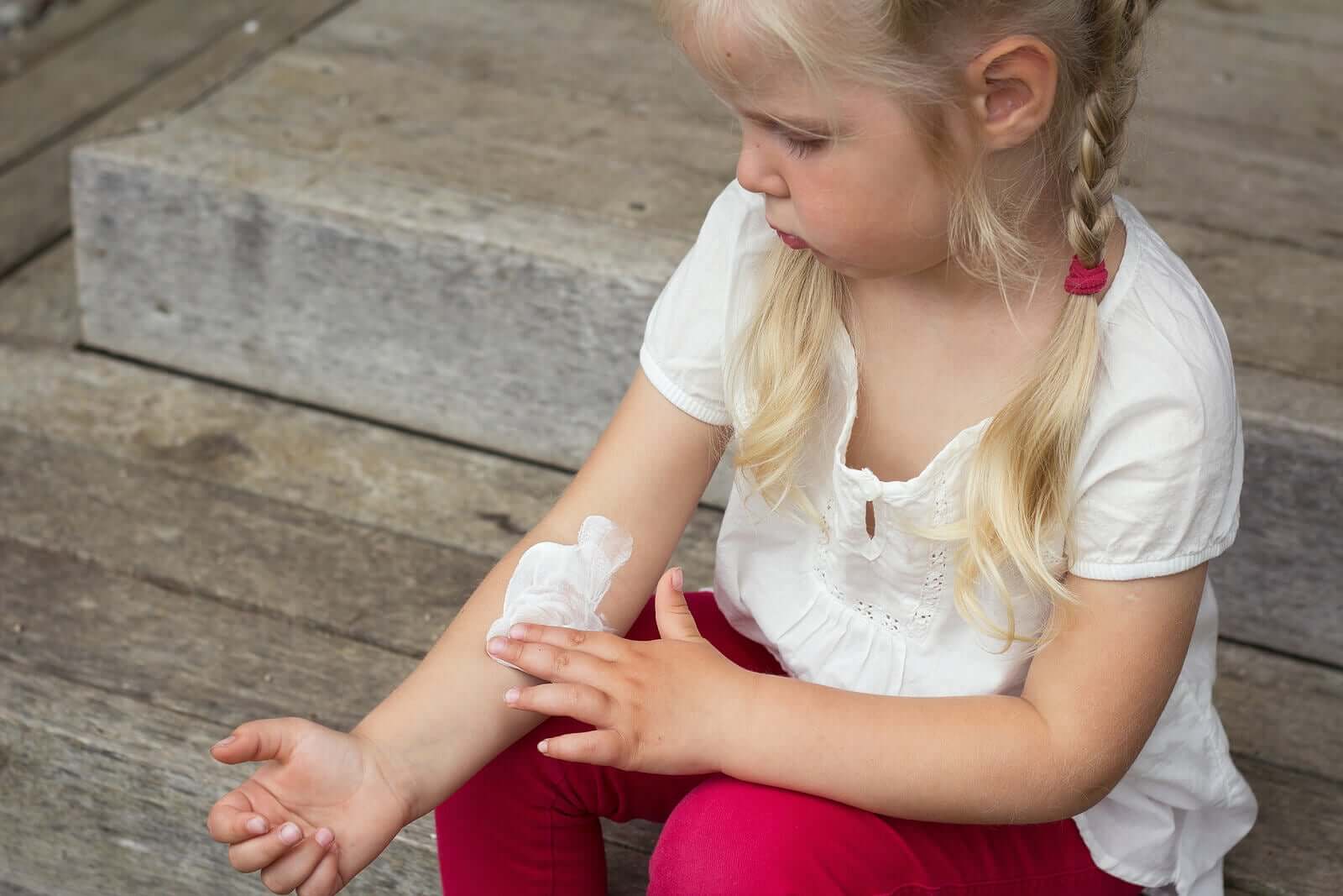A child rubbing lotion on her arm.