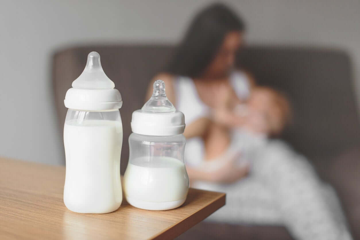 Två nappflaskor som står på ett bord med en mamma som håller sitt barn i bakgrunden.