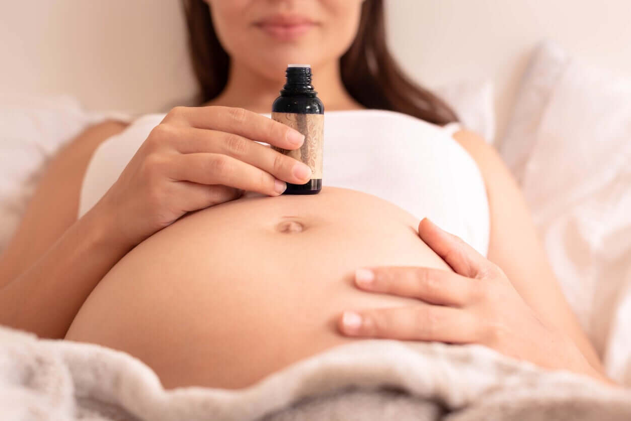 A pregnant woman holding a bottle of massage oil over her belly.