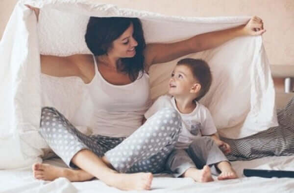 A mother and her toddler son playing under a fort made of a sheet.