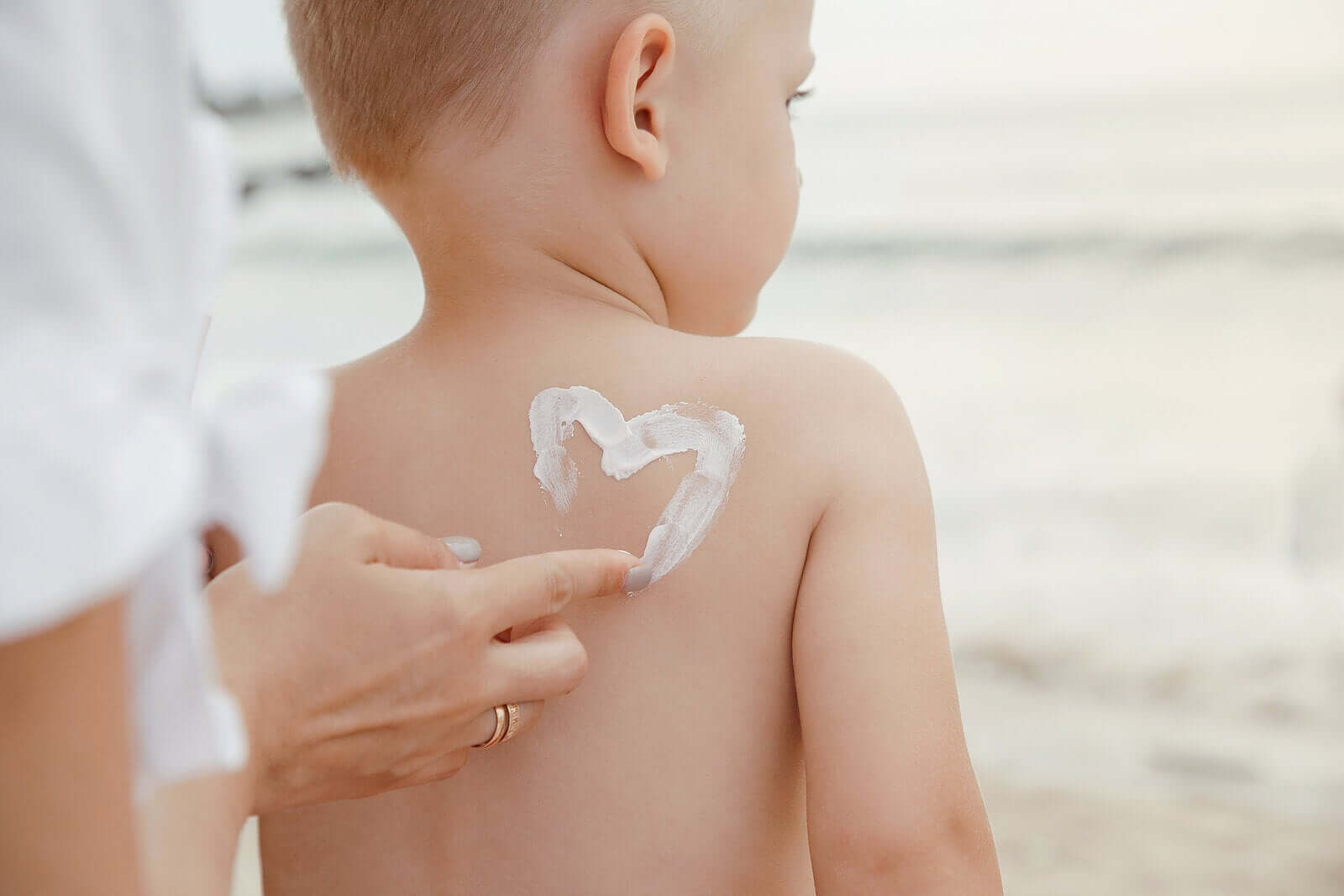 A mother applying sunscreen to her child's back in the shape of a heart.