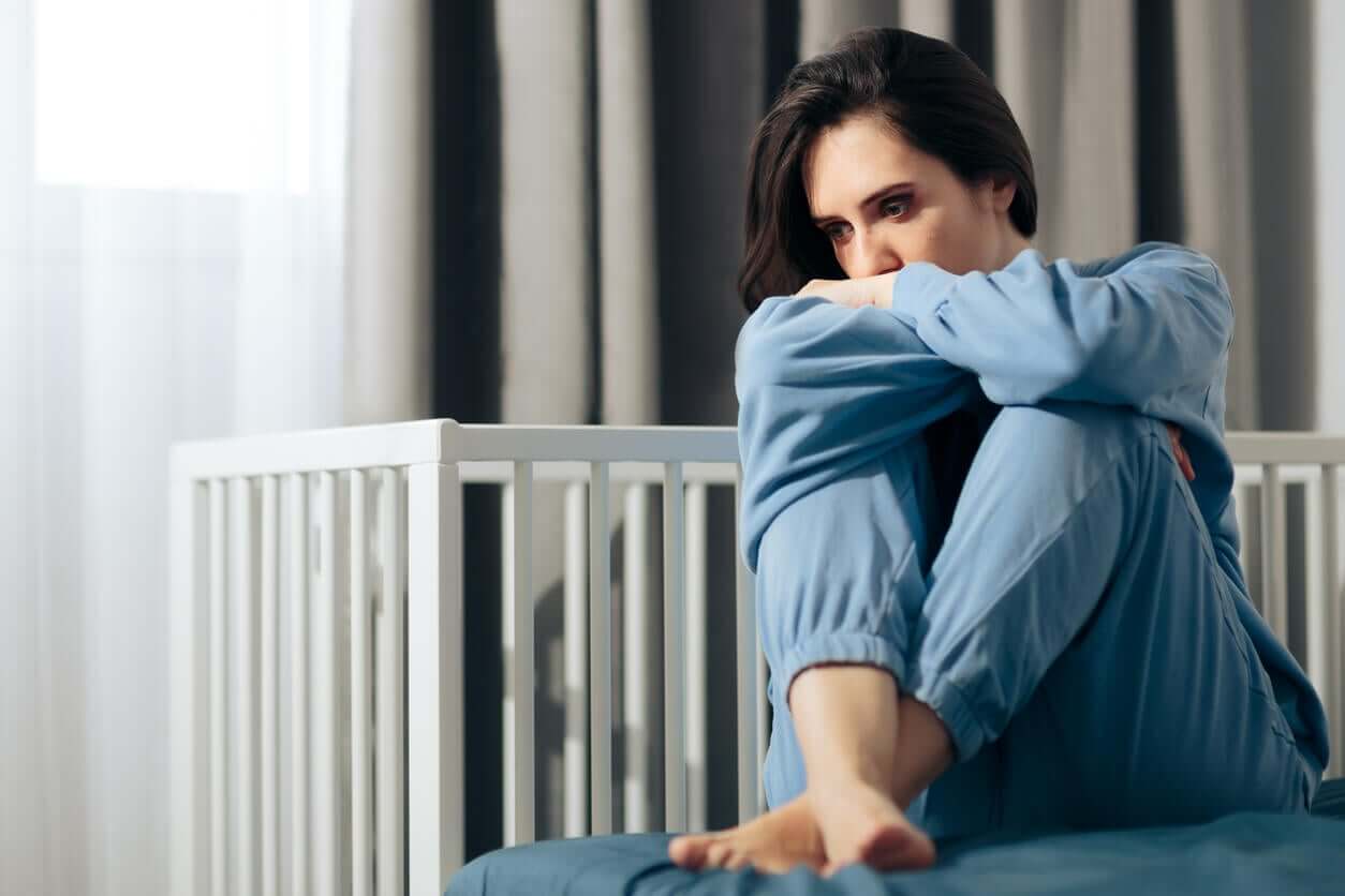 A sad woman sitting near an empty crib.