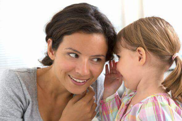 Een klein meisje fluistert iets in het oor van haar moeder