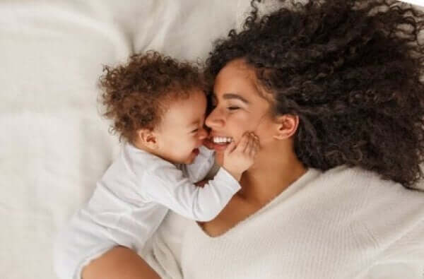 A mother and her baby girling and snuggling in bed together.