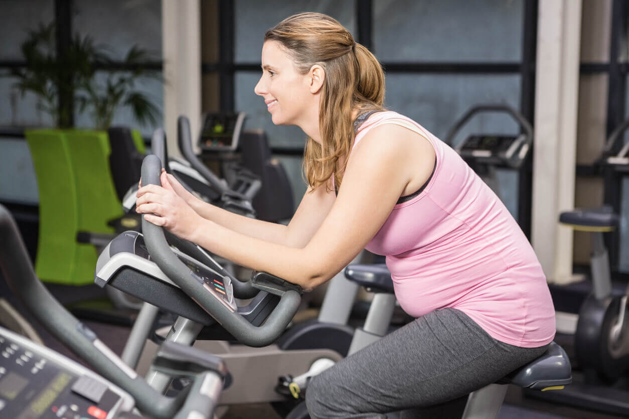 A pregnant woman riding on an exercise bike.
