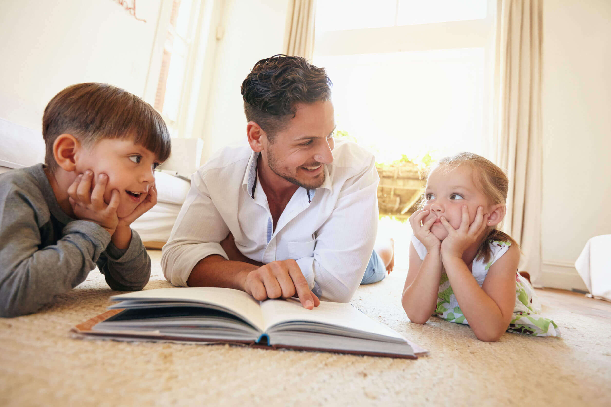 A dad reading on the floor with his son and daughter.