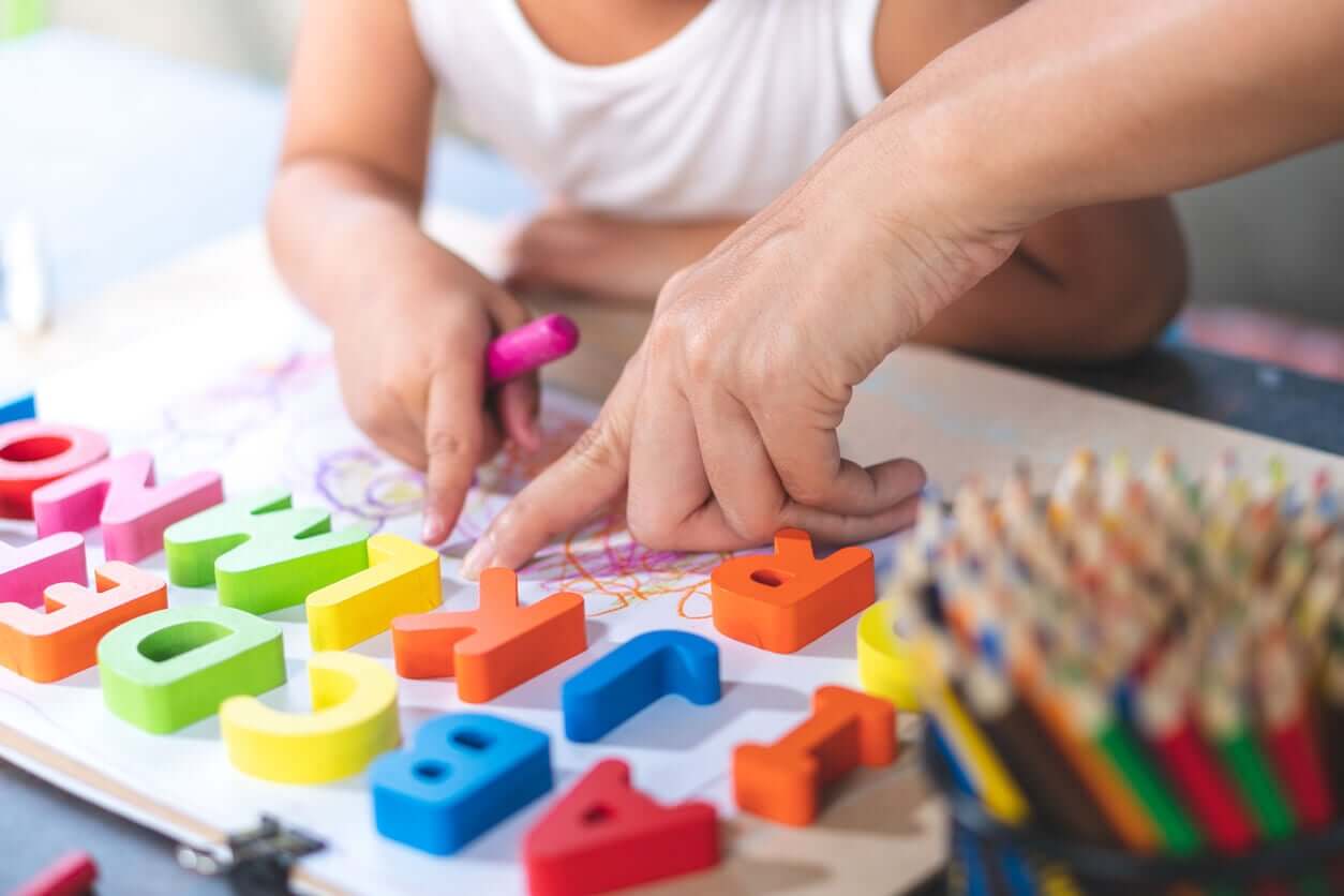 A toddler scribbling on paper while an adult points to the letter L.