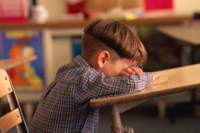 A young boy crying at his desk.