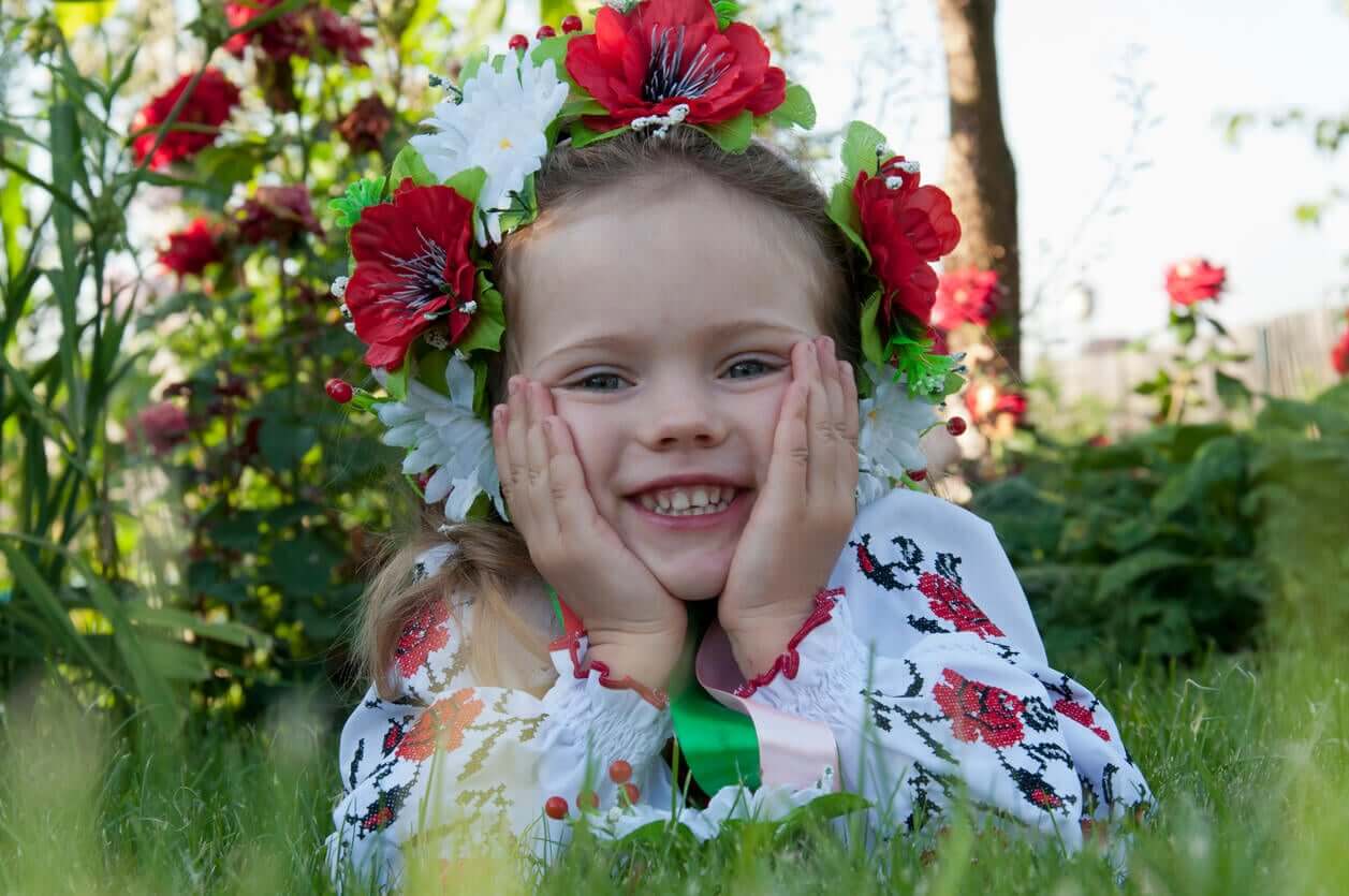 A little girl smiling for the camera with a crown of red and white flowers on her head.