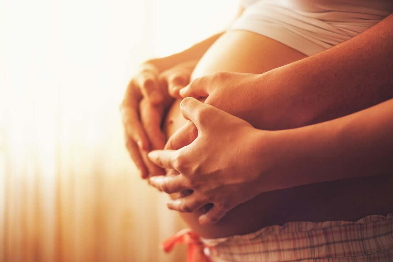 Eine schwangere Frau und ihr Partner umfassen gemeinsam den Babybauch