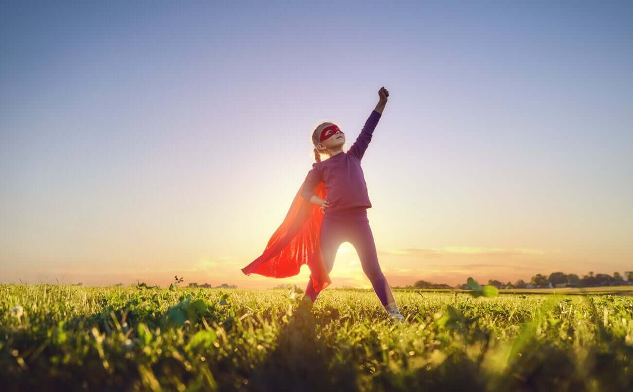 A young girl standing in a field dressed as a super heroin.